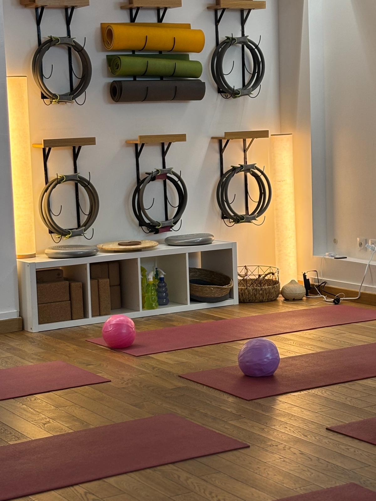 Mur d'accessoires du studio : cercles Pilates, tapis de yoga colorés, briques en liège et ballons