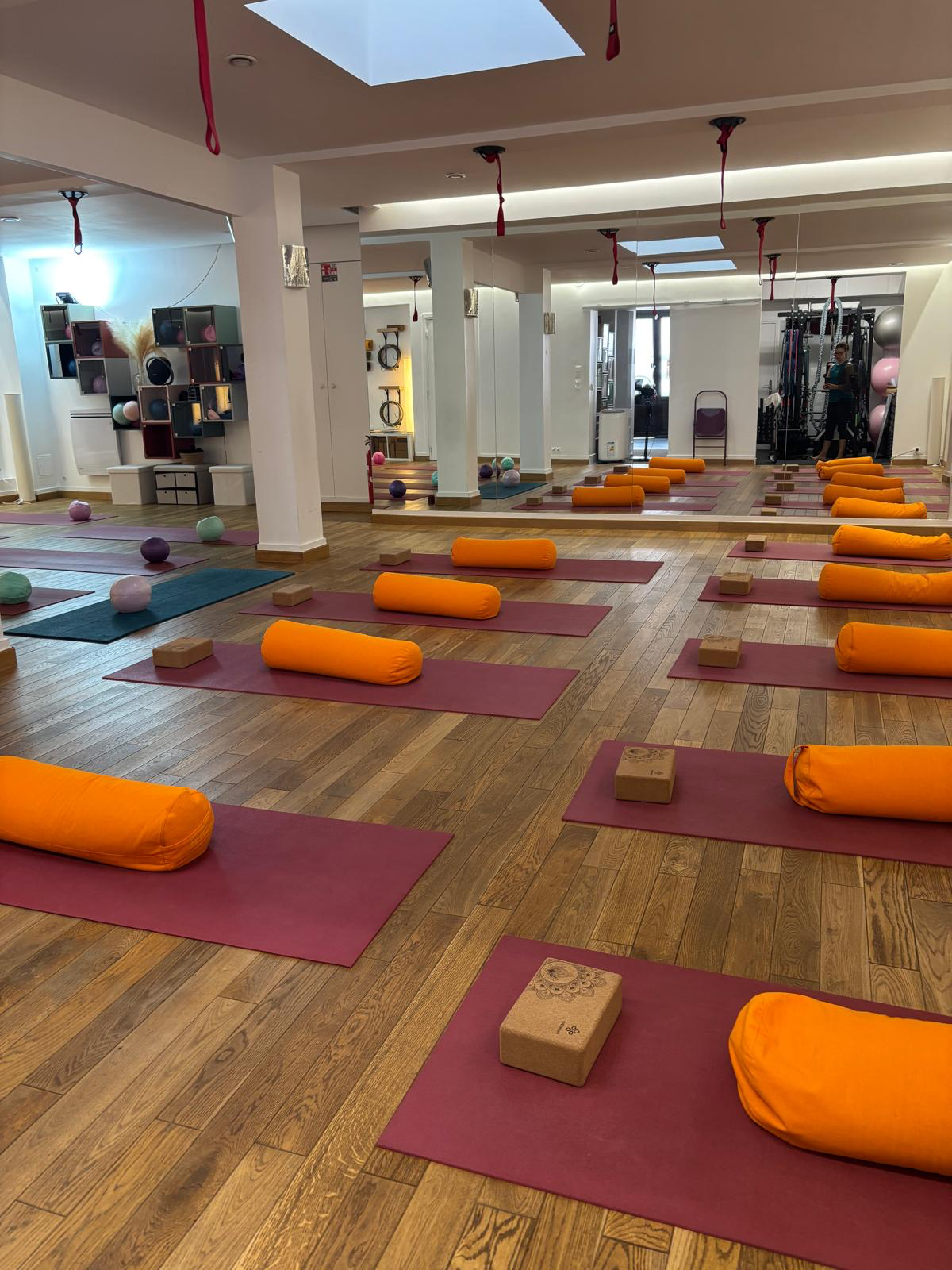 Salle principale du studio préparée pour un cours de yoga avec tapis bordeaux et bolsters orange